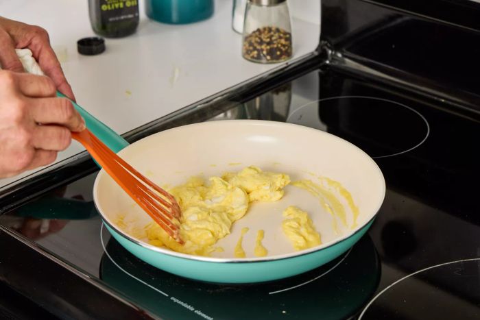 A person uses the GreenPan Rio Ceramic Nonstick 16-Piece Cookware Set to cook eggs in this image.