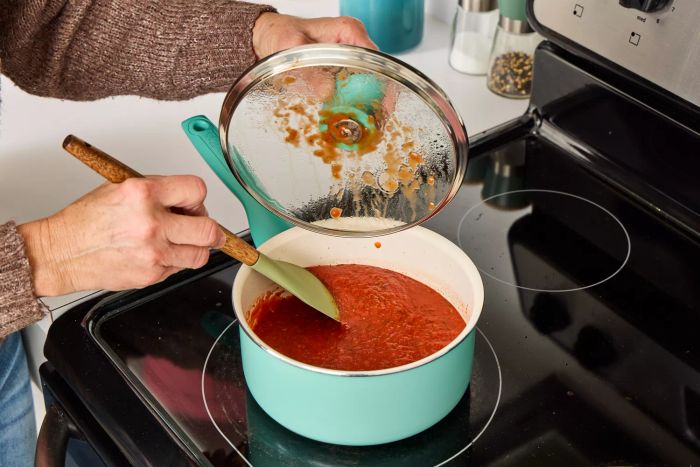 A person prepares red sauce in a pot from the GreenPan Rio Ceramic Nonstick 16-Piece Cookware Set.