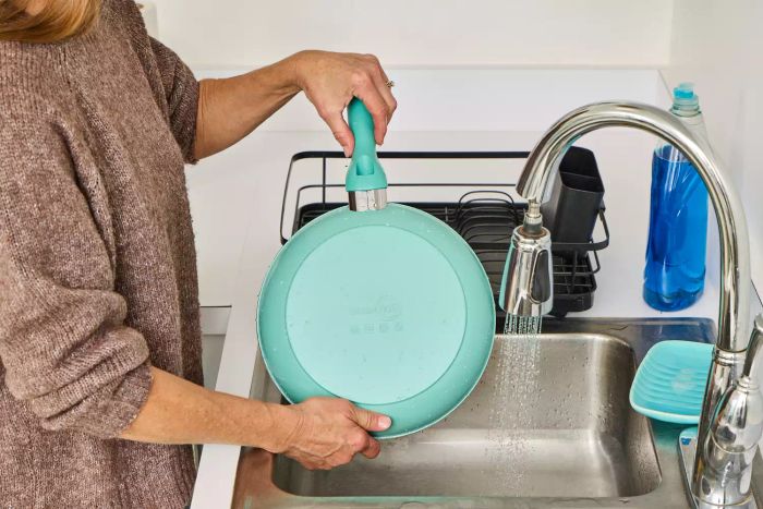 A person cleans the GreenPan Rio Ceramic Nonstick 16-Piece Cookware Set pan.
