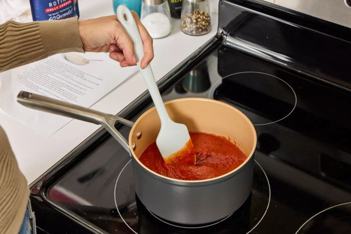 A person stirs tomato sauce inside the Ninja Extended Life Premium Ceramic 9-Piece Cookware Set pot.