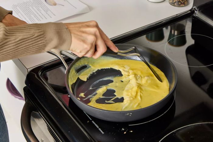 A person prepares eggs in the OXO Ceramic Professional Non-Stick 10-Piece Cookware Set pan.