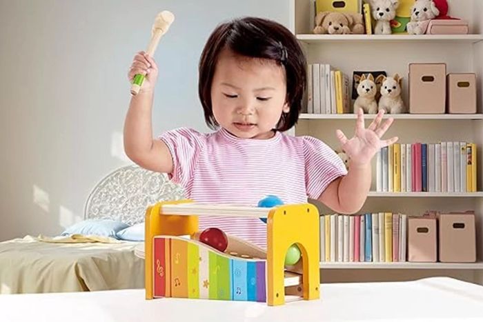 A child plays with the Hape Pound & Tap Bench, which includes a slide-out xylophone, ramps, and balls