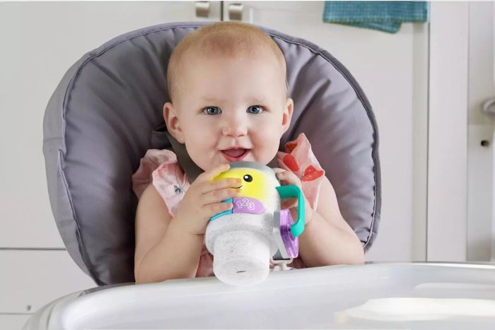 A toddler is seen playing with the Fisher-Price Wake Up & Learn Coffee Mug toy.