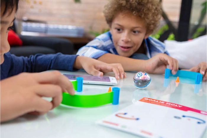 Two children are having fun with the Sphero Mini Activity Kit, guiding a mini-robot through a smartphone