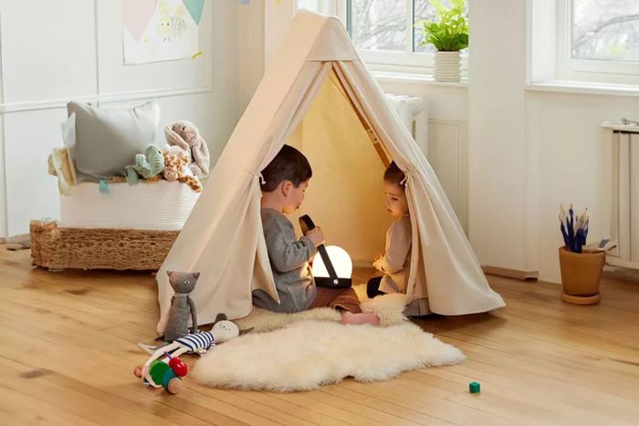 Two children are sitting inside the Lalo Play Tent, with a cozy lamp glowing softly inside.