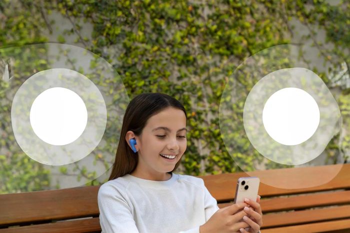 A young girl, wearing the Belkin Soundform Nano Earbuds, smiles as she enjoys music from her phone.