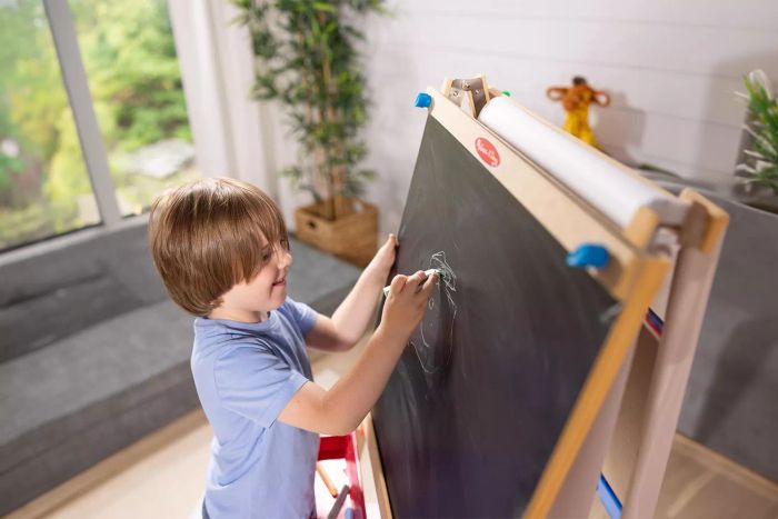 A child is drawing on a Melissa & Doug Deluxe Standing Easel.