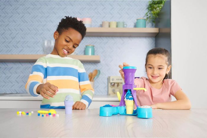 Two kids are having a blast playing with the Kinetic Sand Soft Serve Station.