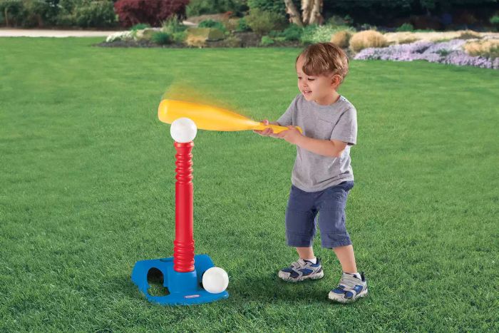 A child is enjoying a game with the Little Tikes T-Ball Set on a grassy outdoor lawn.