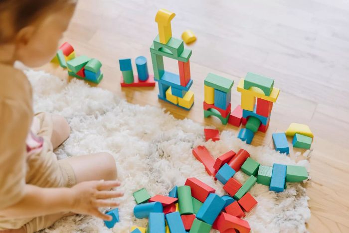 A child is having fun with the Melissa & Doug Wooden Building Blocks 100-Piece Set, constructing towers on a soft rug.