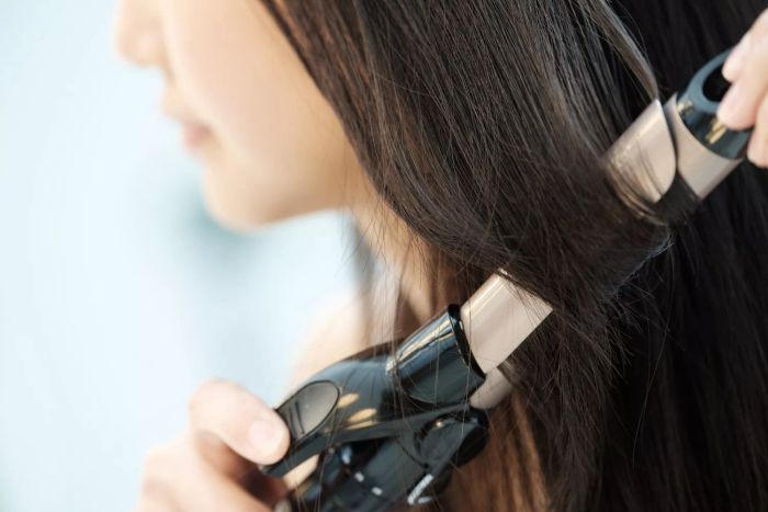 A woman using a curling iron to style her hair