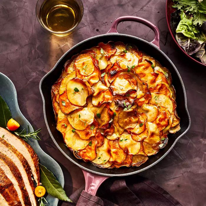 These golden, garlicky herb-butter layered potatoes are served in a cast-iron dish, beautifully arranged alongside other festive dishes on the table.