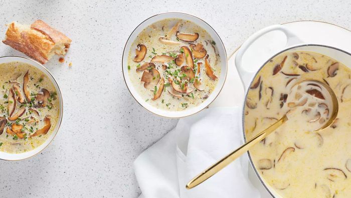 Creamy Mushroom Soup With Chives in a Deep White Pot With a Metal Ladle for Serving, Surrounded By Two Bowls of Soup and Bread