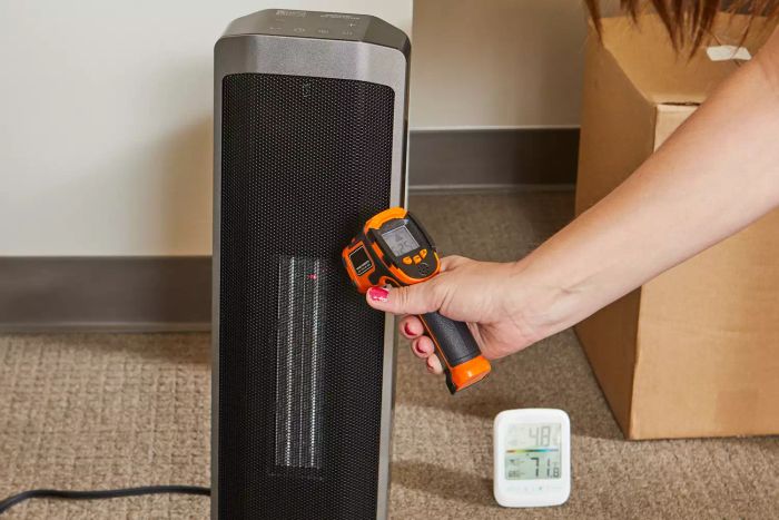 A person measuring the temperature of the Better Homes & Gardens 23-Inch Electric Ceramic Tower Heater
