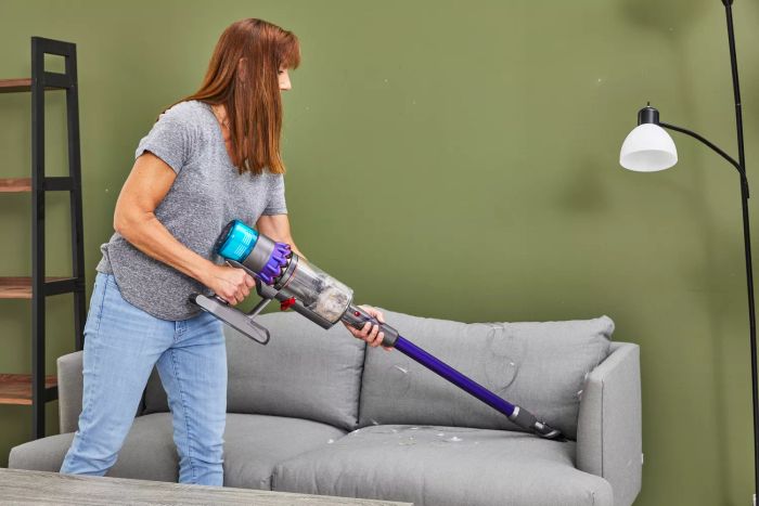 A person using the Dyson Gen5detect Cordless HEPA Vacuum to clean a sofa in a living room.