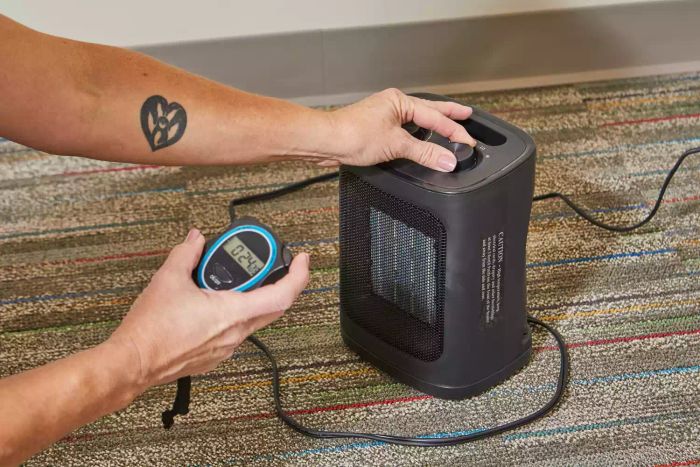 One hand adjusting the knob on the Kismile Space Heater while the other holds a stopwatch