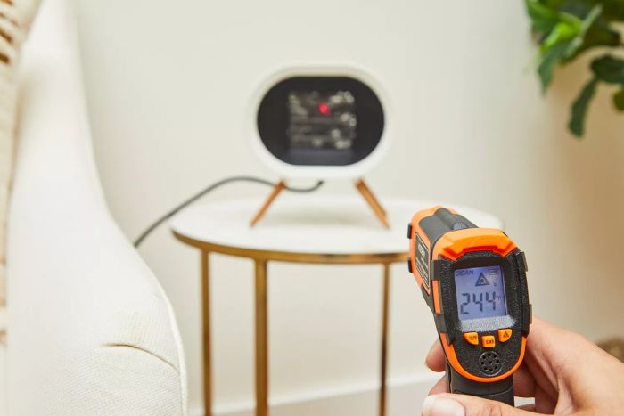 A person measuring the temperature of the BabyExo Small Space Heater using an infrared thermometer