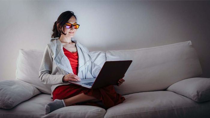 woman wearing blue-light blocking glasses and using a laptop