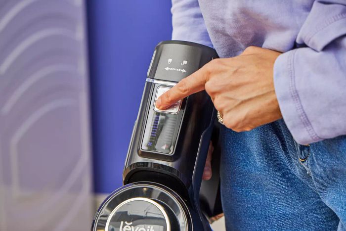 A finger pressing a button on the Levoit VortexIQ 40 Cordless Stick Vacuum.
