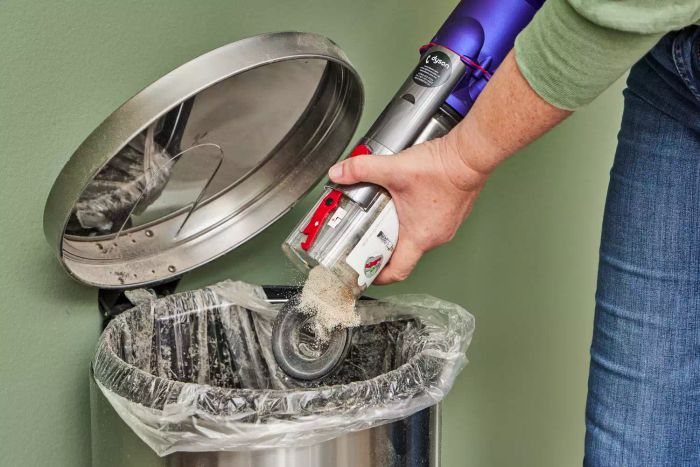 A person is disposing of dust and debris from the Dyson Omni-Glide Cordless Vacuum into a trash can.