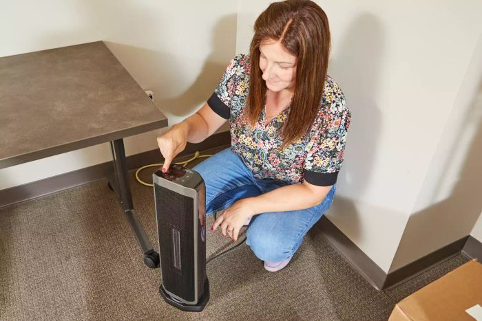 A person adjusting the settings on the Better Homes & Gardens 23-Inch Electric Ceramic Tower Heater