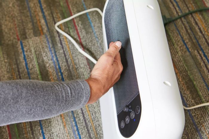 The back of a hand touching the Honeywell ThermaWave 6 Ceramic Technology Space Heater which is sitting on a carpeted floor