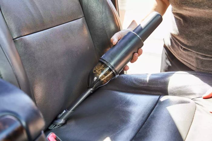 Hand using the Bissell AeroSlim Cordless Handheld Vacuum to clean a car seat