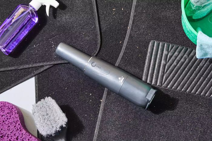 Bissell AeroSlim Cordless Handheld Vacuum resting on the car floor next to other cleaning tools