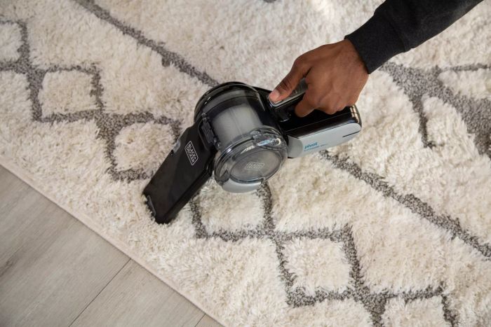 A person is seen vacuuming a carpet with the BLACK+DECKER 20V Max Handheld Vacuum, Cordless, Grey (BDH2000PL).