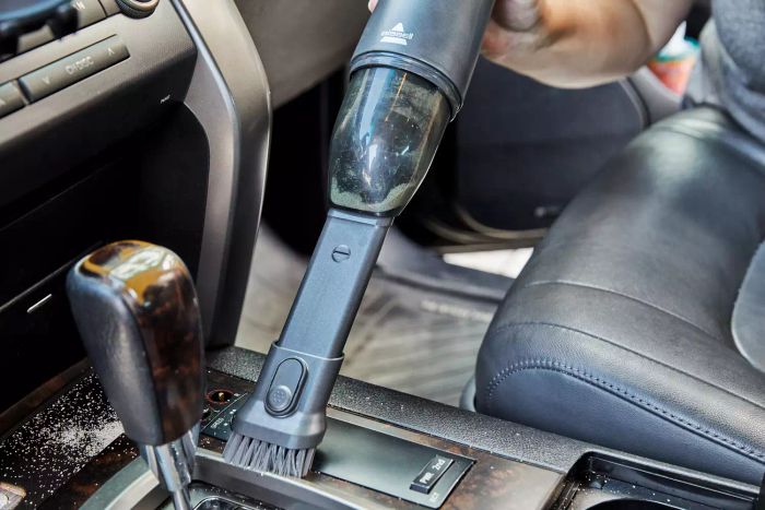 Hand using the Bissell AeroSlim Cordless Handheld Vacuum to clean the car console