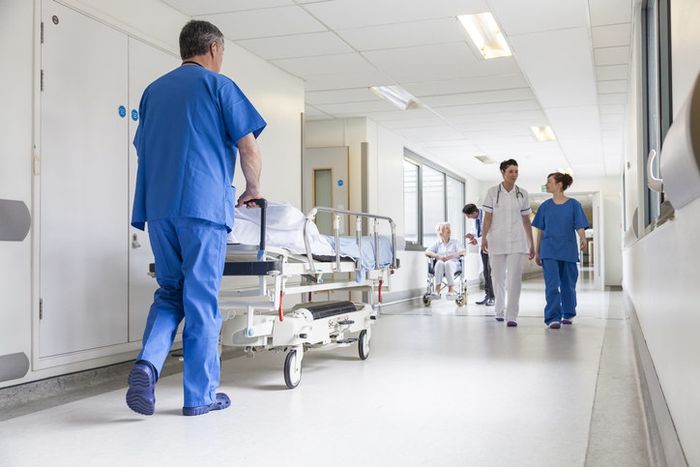 A male nurse pushing a stretcher with a senior female patient and doctors in a hospital hallway