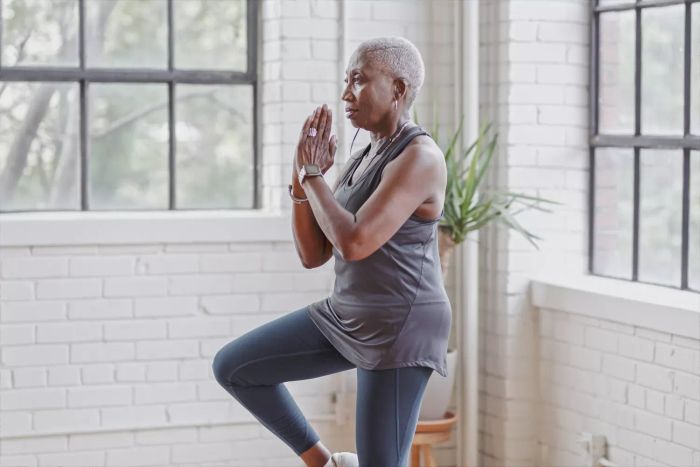 A woman demonstrating a one-legged balance in a yoga pose with her hands clasped together.