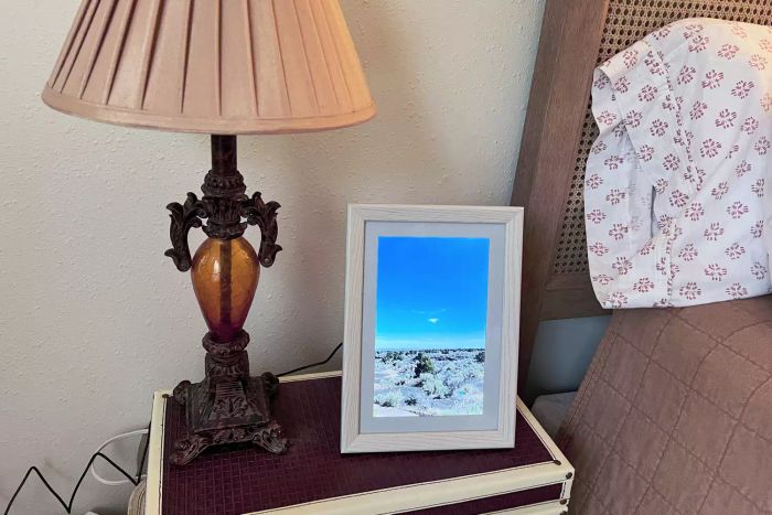 The Aeezo WiFi Digital Picture Frame positioned in portrait orientation on a bedside table.