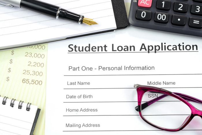 Filling out a student loan application with a calculator, pen, and notepad on the desk.