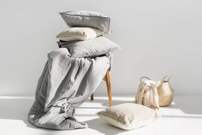 A plaid design resting in a wicker basket, accompanied by a fresh blanket, linen bedding, cotton sheets, a pillow, a cushion, and a duvet made from natural materials laid over a chair after laundering, with ample copy space. This illustrates the essence of washing, home maintenance, and hotel-grade service.