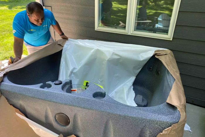 A person leans over the Aquarest Spas Select 150 4-Person 12-Jet Rectangular Plug-and-Play Hot Tub while setting it up.