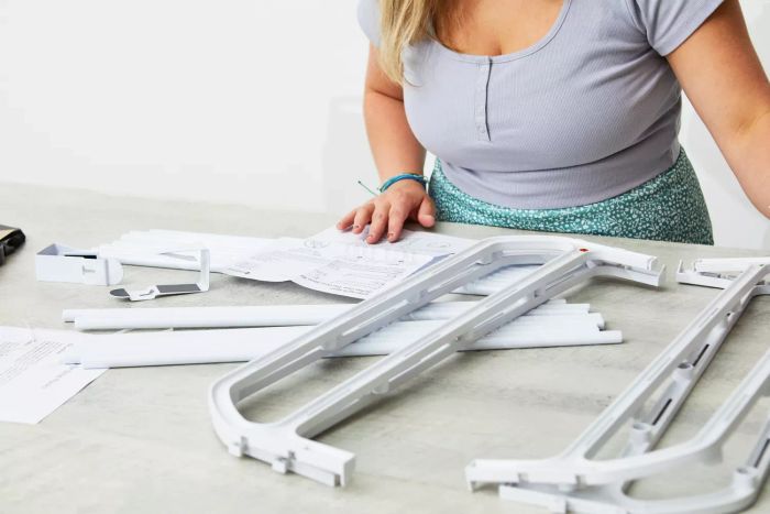 A person assembling the Whitmor Over-the-Door Shoe Rack while reviewing the instruction manual on a table