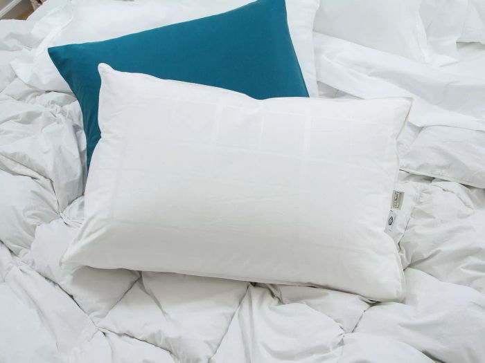 The L.L.Bean Sateen White Goose Down Pillow resting on a white comforter with a teal pillow alongside it.