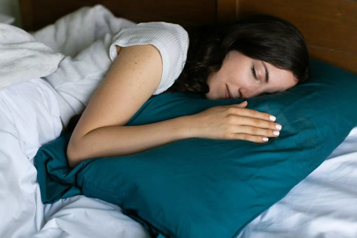 A woman resting on a Boll & Branch Down Chamber Pillow, with a blue pillowcase on the bed