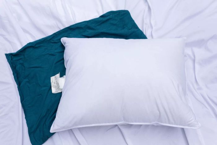 The Helix Down & Feather Pillow resting on a bed with white sheets and a blue pillowcase.