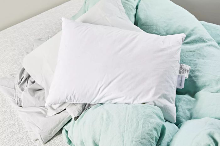 The Boll & Branch Down Pillow placed on a green comforter and white sheet.