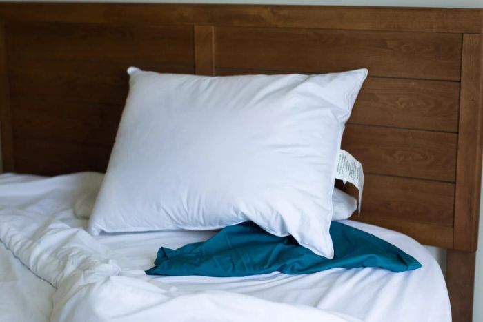 The Helix Down & Feather Pillow placed on a bed with crisp white linens and a blue pillowcase.