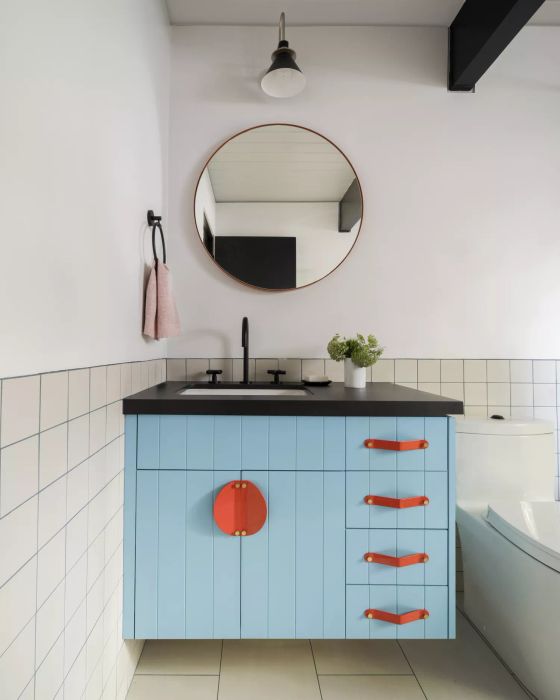 a bathroom featuring a blue vanity paired with orange hardware accents