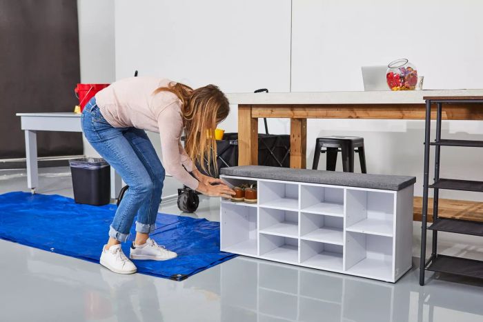 A person organizing shoes in the assembled VASAGLE Shoe Bench placed on grey flooring beside a blue tarp