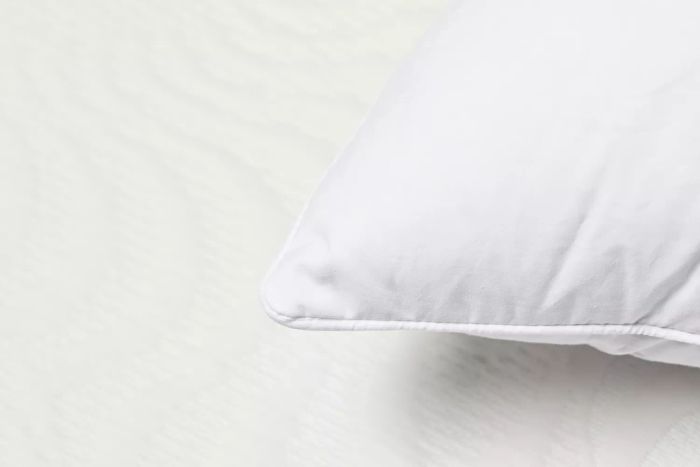 A closeup view of the corner seam of the Boll & Branch Down Pillow resting on a white mattress.