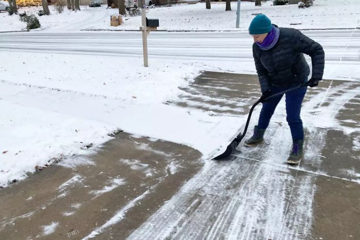 A person shoveling a driveway with the Suncast SC3250 18-Inch Snow Shovel/Pusher Combo