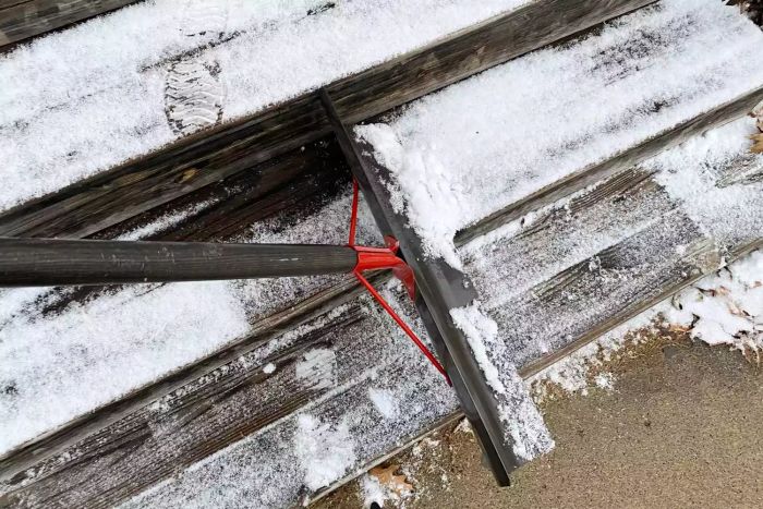 A person clears snow from wooden steps using the Garant NSP24D Nordic 24-Inch Steel Blade Snow Pusher.