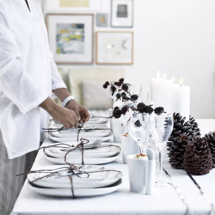 Design a Christmas table with a white and silver theme, featuring plates, candles, and pinecones