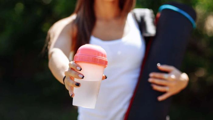 A woman holding a shaker filled with clear whey.