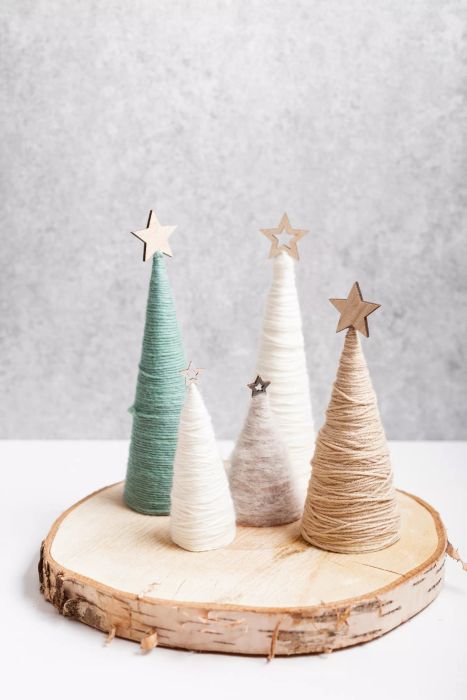 A Christmas craft background featuring handmade yarn cone Christmas trees in natural hues. A DIY sustainable decoration idea for an organic holiday spirit.